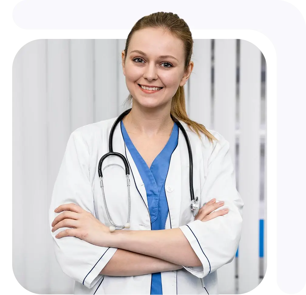 Female medical professional in a white coat with a stethoscope, smiling and standing with arms crossed.
